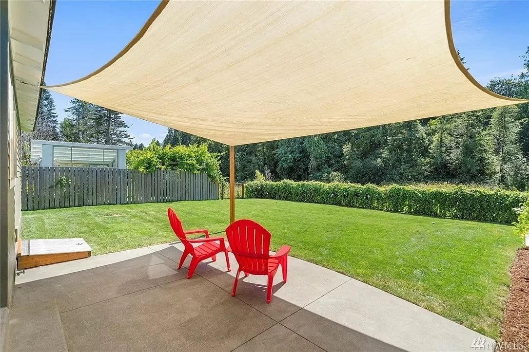 A patio with two red chairs under an umbrella.